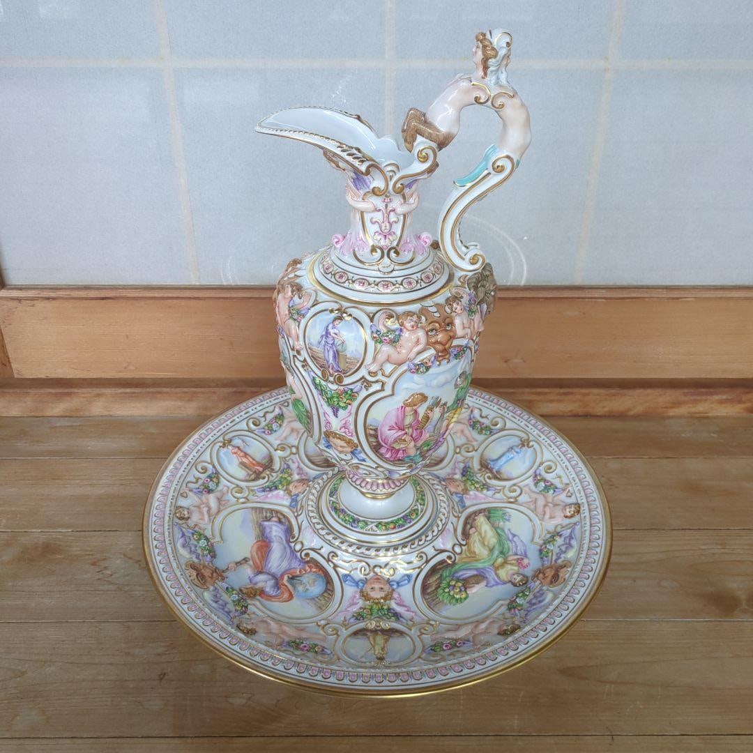 Richard Ginori Capodimonte: The Myth of the Jug: - Color: Multi-colored (primarily white, gold, pink, and blue) - Decoration: Decorative pattern and gold leaf - Design: The handle features a female figure - Shape: Jug and plate set - Era: Antique -