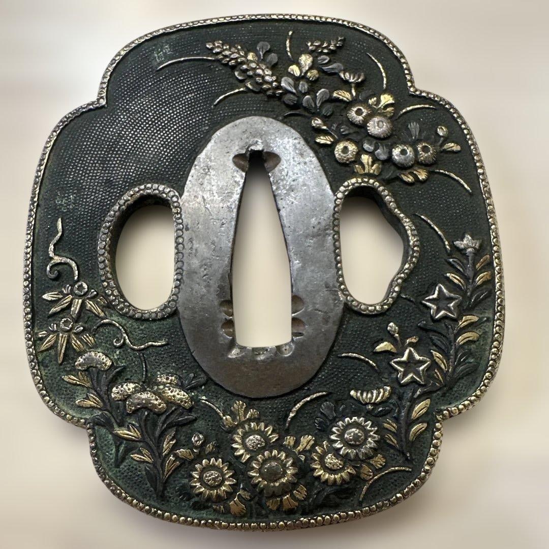 Sword Fittings – Tsuba (Hand Guard) with Autumn Grass Motif: A finely crafted Japanese tsuba featuring delicate floral and plant decorations inspired by autumn grasses. This ornamental hand guard exemplifies traditional metalworking artistry and is ideal for co