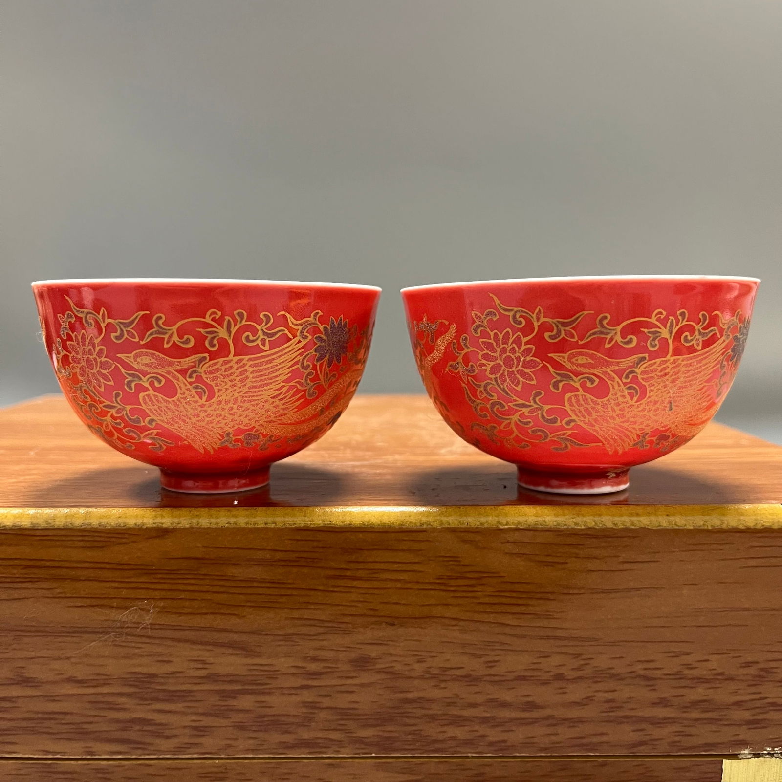A pair of red-ground gilt-painted porcelain cups with double phoenixes and lotus patterns from the: A pair of porcelain cups from the Chenghua period of the Ming Dynasty, decorated with a red ground and gilt design of phoenixes and lotus scrolls, each measuring 4.5 x 8 cm.The cups are thin and light
