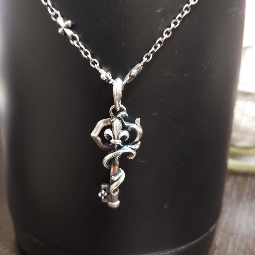 (Second-hand) Silver 925 Lily Flower Key Pendant Necklace: This 925 silver necklace is decorated with a key and iris flower pattern, and comes with a rope chain. Material: 925 silver Design: Key and iris flower pattern Chain type: Rope chain with cross and li