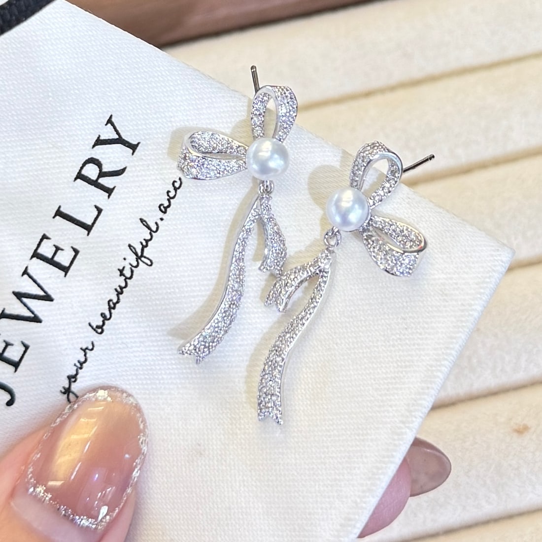 Freshwater Pearl Earrings: This pair of earrings showcases the allure of 5-6mm freshwater pearls, known for their perfect roundness and intense luster. These high-quality pearls are complemented by a chic bow design, adding a t