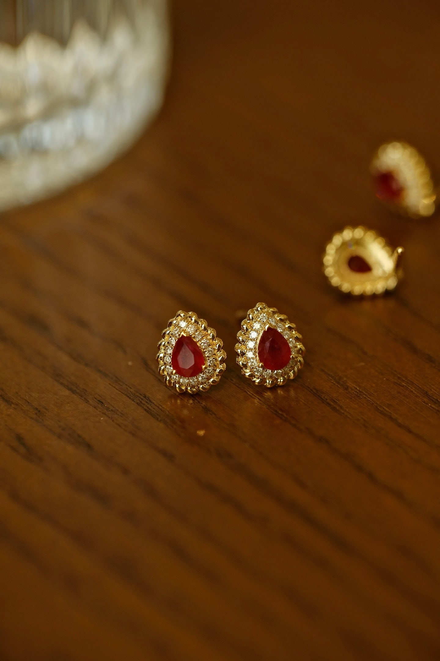 18K Gold Ruby Earrings: This pair of 18K Gold Ruby Earrings embodies a captivating allure with its natural pigeon blood red hue, elegantly framed by a sparkling diamond halo. The vintage-inspired twisted edge design adds a