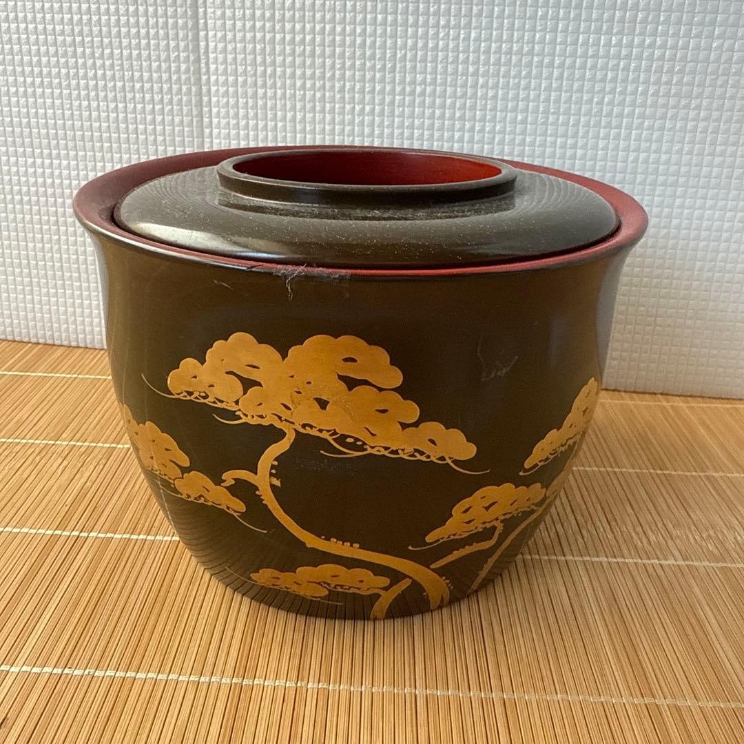 Black and gold pine tree pattern water container: This is a black and gold sake cup coaster with a pine tree pattern on it.Color: Black with gold accents.Design: Pine tree pattern with a crane design on the lid.Shape: Circular water container.