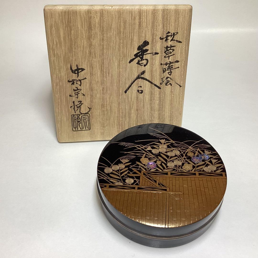 A circular incense box designed by Nakamura SOetsu, decorated with maki-e (gold lacquer) and: This is a circular incense box crafted by Nakamura SOetsu, utilizing autumn grass lacquer and mother-of-pearl inlay techniques, housed in a wooden box. It is a tea ceremony utensil as well as an antiq