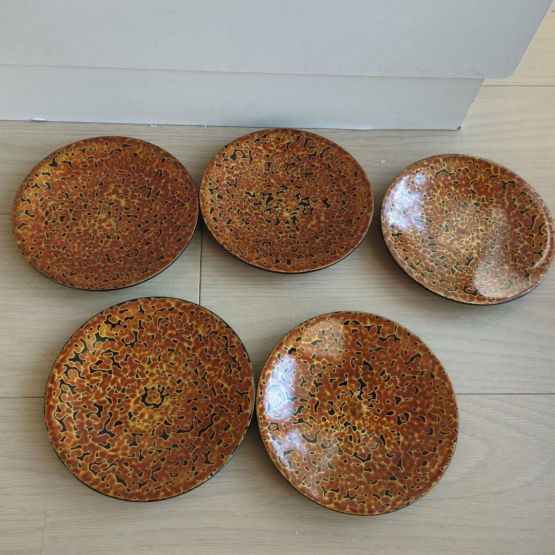 A set of five circular gilt lacquer plates.: A circular plate featuring abstract patterns in orange and black. Color: Orange and black patterns Shape: Circular Reverse: Glossy black Design: Abstract patterns Dimensions: Approximately 14 cm in di