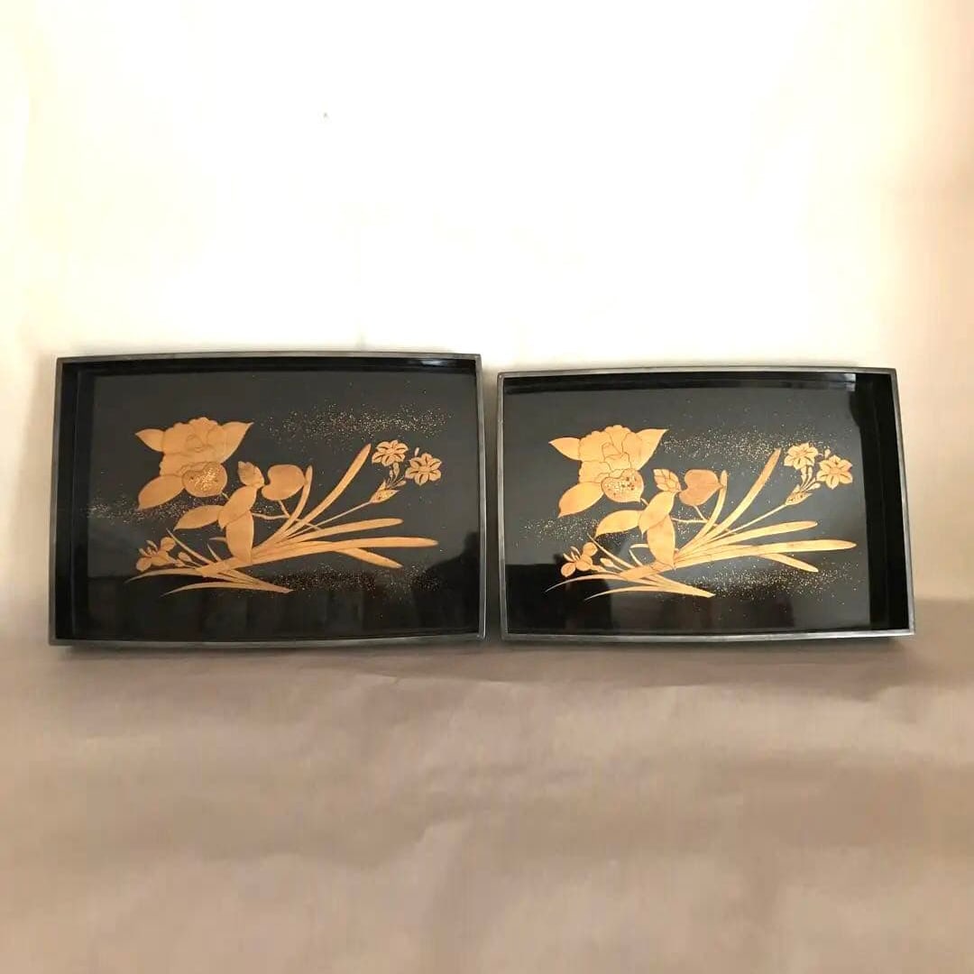 Square Lacquer Trays with Floral Patterns (Large and Small): This is a set of two square trays, one large and one small, adorned with maki-e (lacquerware) floral patterns. The front design features irises, camellias, and daffodils. Both trays show signs of use,