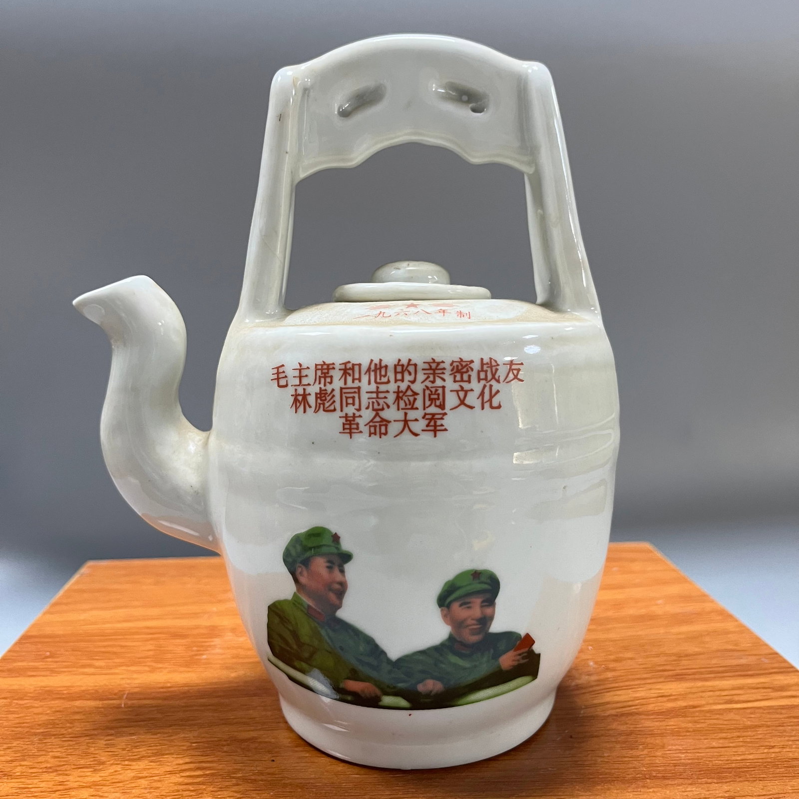 Porcelain teapots from the Cultural Revolution period: This is a porcelain teapot with a handle, made in 1968 during the Cultural Revolution, with a political propaganda theme. It measures 20 x 15.5 cm. The teapot has a straight cylindrical body, is glaze