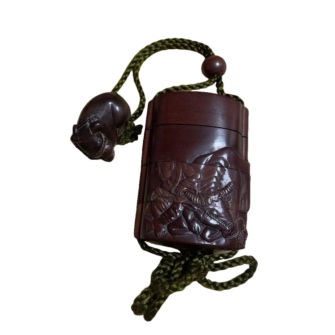 Wooden inrO, carved with a design of oxen.: Wooden inrO, carved with a motif of oxen. Material: Wood Design: Sculpture Color: Brown String Color: Green Dimensions: Approximately 10 cm x 6 cm