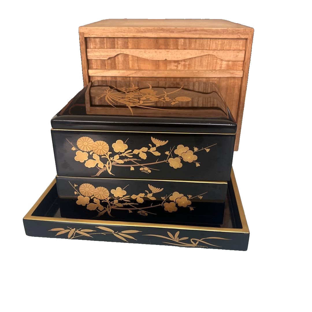 A double-layered bento box with a stand, the interior adorned with exquisite red and black lacquer,: This is a Wajima lacquer bento box. The elegant red and black lacquer interior walls are complemented by exquisite gold inlays of the Four Gentlemen motifs. The design is very delicate, with clear dep