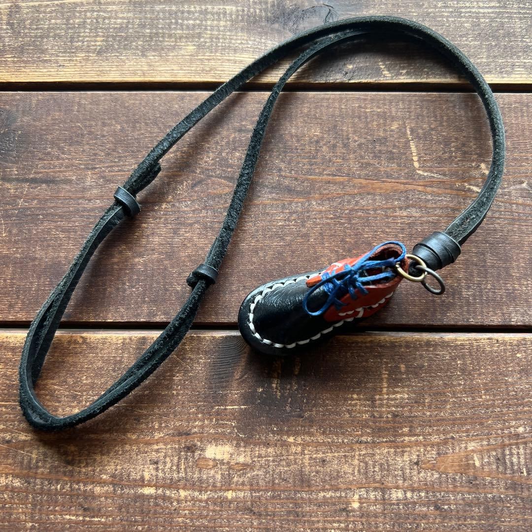 Second-hand - Mini leather shoe-shaped pendant, with adjustable strap.: A brown and black leather shoe-shaped pendant with an adjustable strap. Pendant size: 5.5 cm. Design: Shoe-shaped pendant Color: Black and brown combination Material: Leather Strap length: Adjustable 