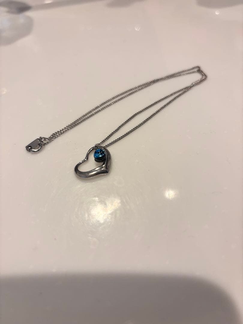 Second-hand - Heart-shaped pendant necklace, set with blue gemstone (from Okinawa): A beautiful necklace with a heart-shaped pendant, set with a blue gemstone. Design: Heart-shaped pendant Material: Silver metal Decoration: Blue gemstone Chain type: Fine chain Clasp type: Lobster cla
