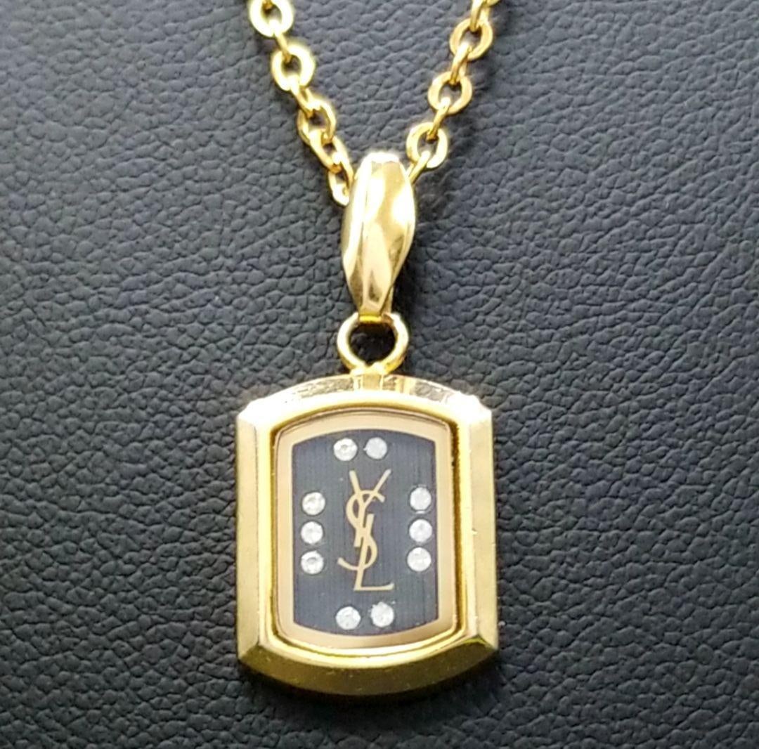 Second-hand - Saint Laurent square gold necklace, vintage style: This YSL (Yves Saint Laurent) necklace features a delicate design with the brand's classic logo and gemstone embellishments elegantly accentuating the neckline. The golden shine adds a touch of luxury
