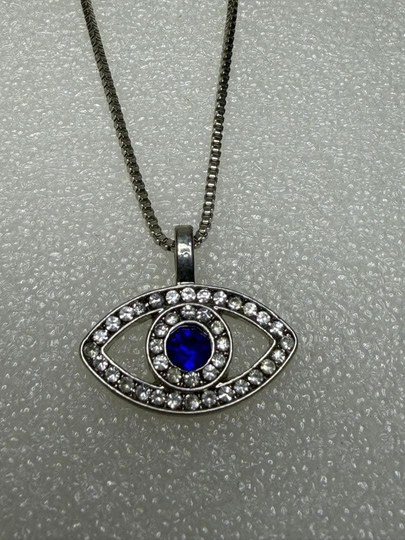 Second-hand - Sapphire eye-shaped necklace: Eye-shaped necklace adorned with blue gemstones and crystals, featuring an adjustable chain. Design: Eye-shaped pendant Stones: Blue gemstones and crystal embellishments Color: Silver Chain Length: