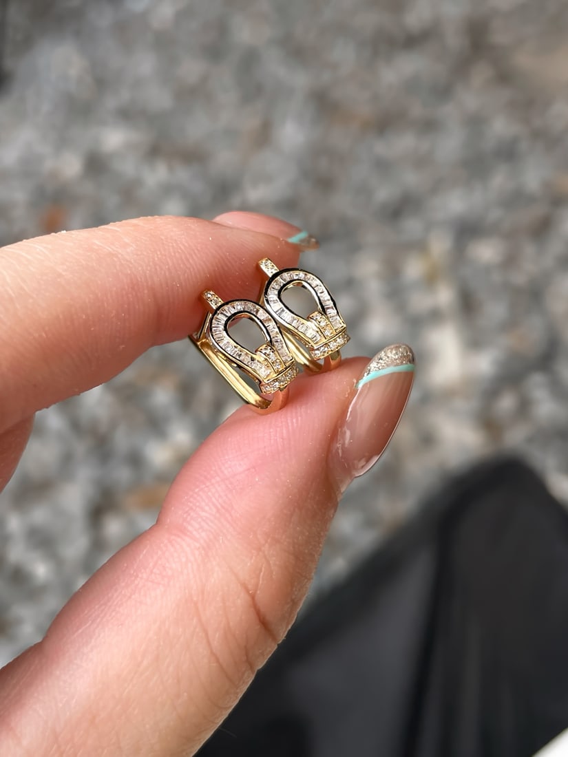 A pair of 18K gold diamond earrings.: This pair of 18K gold diamond earrings is designed with the classic horseshoe buckle element, showcasing an eternal and faultless elegance. The step-cut diamonds set on the earrings sparkle like dazzl