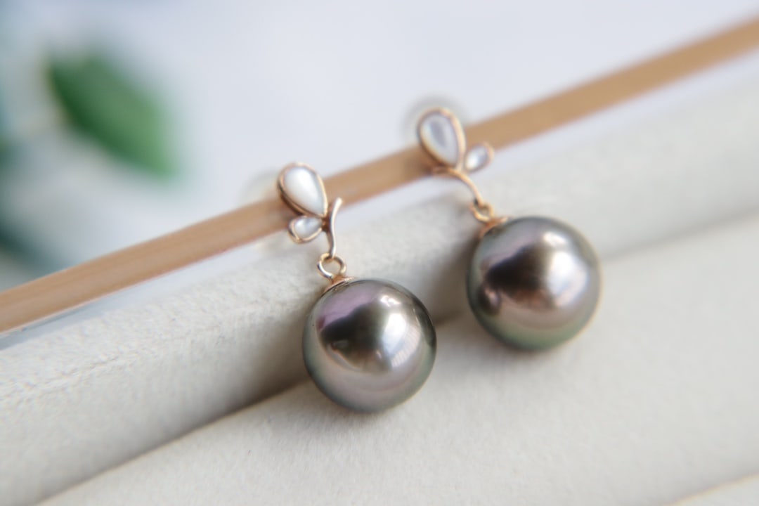 18K gold Tahitian pearl earrings: This 18K gold Tahitian pearl earrings, with its perfect round shape and strong luster, attracts every eye. The pearls exhibit a charming peacock green overtone, and the slightly flawed surface