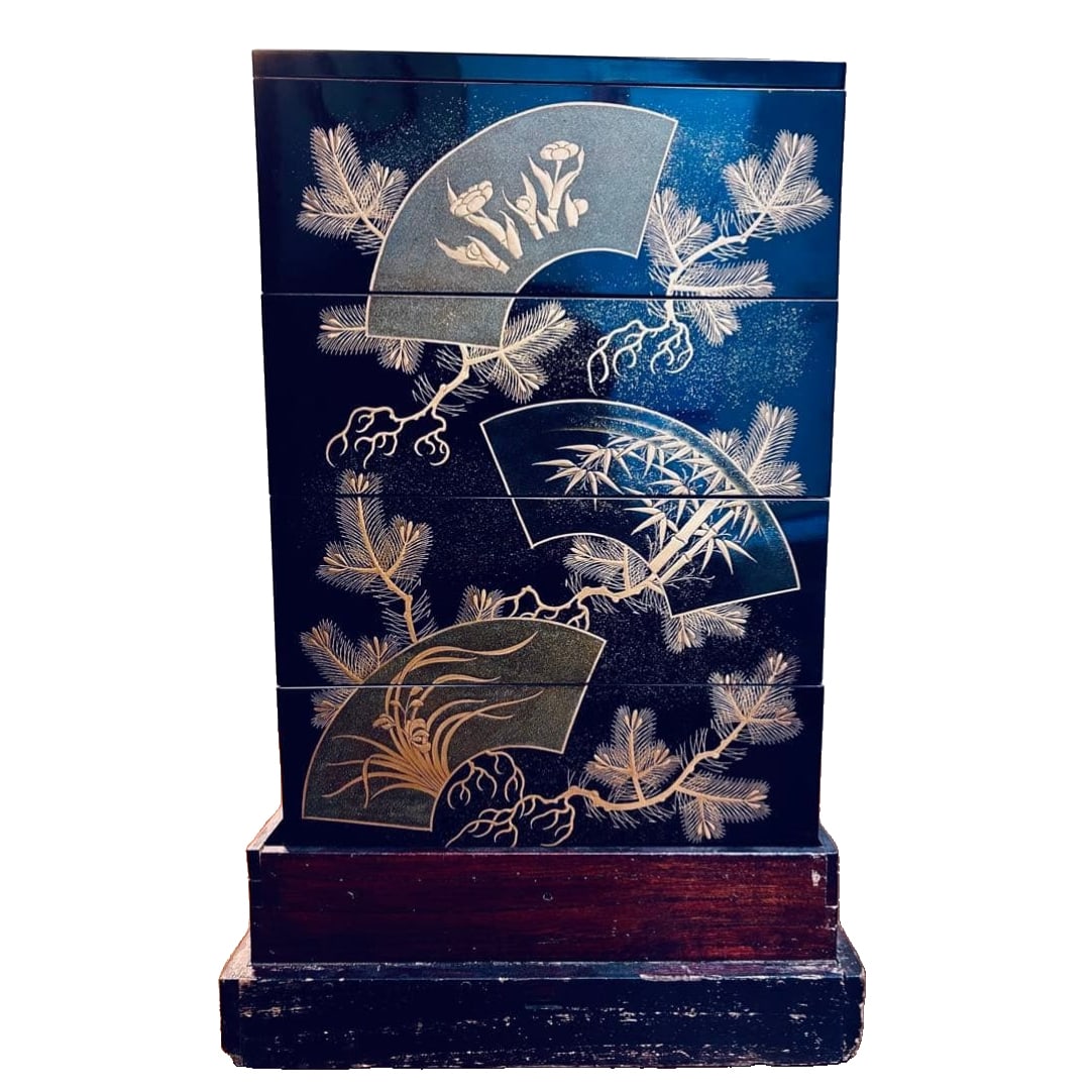 Antique four-tier lacquer box, featuring a black lacquer fan-shaped design adorned with motifs of: This is a four-tiered bento box, with a black lacquer base adorned with gold maki-e, featuring a design of fan-shaped pine trees, bamboo, plum blossoms, and chrysanthemums. The design prominently show