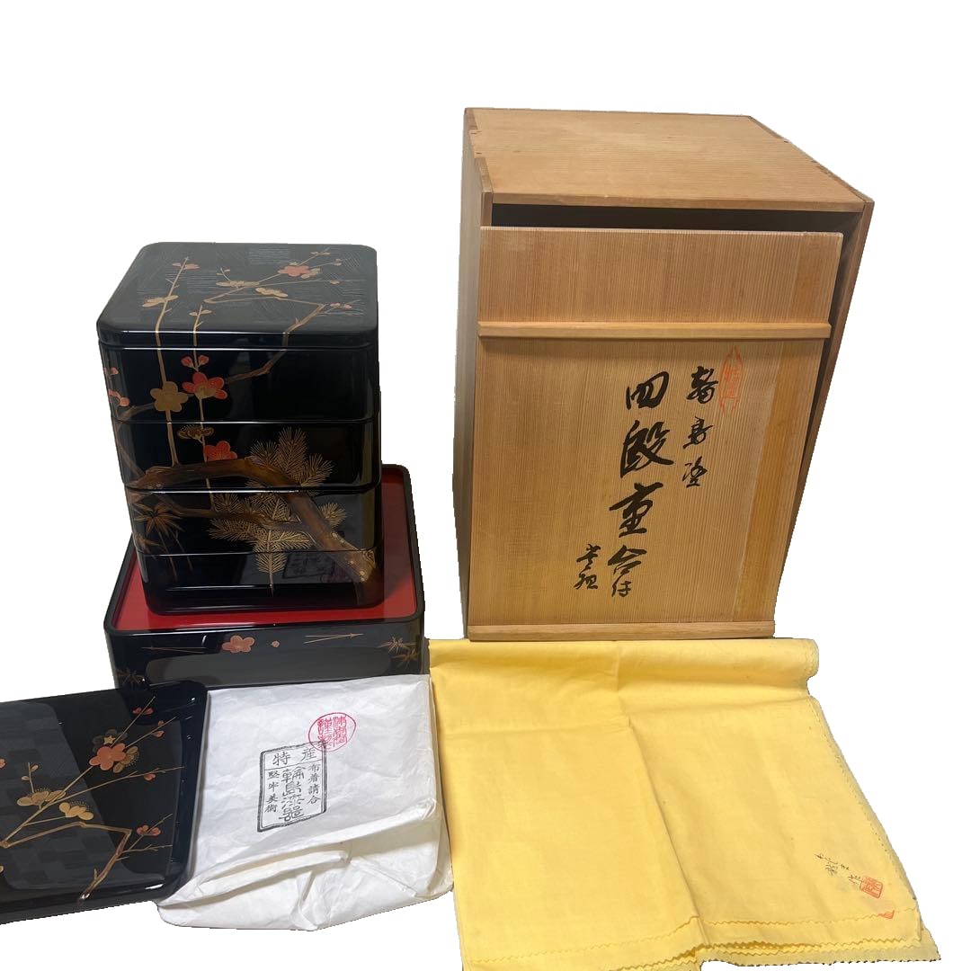 Lacquered bento box, four-tiered set, adorned with gold leaf.: A finely crafted four-tier lacquered bento box, adorned with gold leaf depicting patterns of pine trees, bamboo, and plum blossoms. Material: Lacquerware Color: Black, Red Decoration: Gold leaf floral