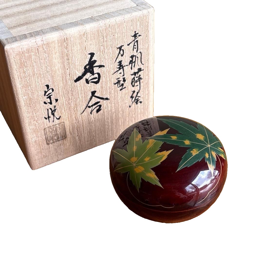 A blue maple leaf maki-e incense box in the shape of a bun, made by Nakamura Soetsu, crafted from: A blue maple leaf maki-e incense box in the shape of a bun, made by Nakamura Soetsu, crafted from cherry wood with a lacquer finish, accompanied by the original box, suitable for tea ceremony use. It 