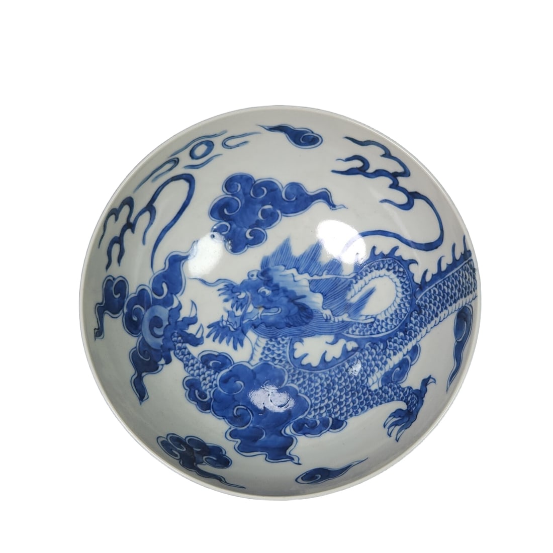 Qing Dynasty Kangxi period blue and white dragon bowl with overpass design.: This Qing Dynasty Kangxi period blue and white dragon bowl has a solemn shape, with a slightly flared rim, a spacious body, and a well-proportioned foot. The blue and white color is rich, displaying t