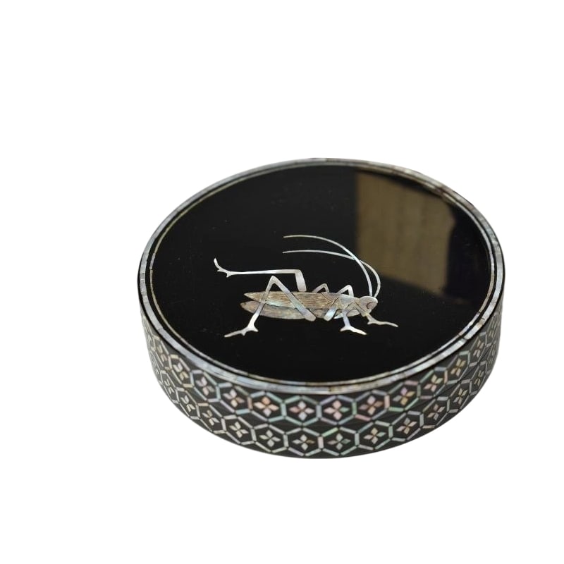 A mother-of-pearl cricket-patterned incense box designed by Suzuki Mitsunari, accompanied by the: A mother-of-pearl cricket motif incense box designed by Suzuki Mitsunari, accompanied by the original box. There is some minor wear. Dimensions: Height: 2 cm, Width: 8.3 cm.