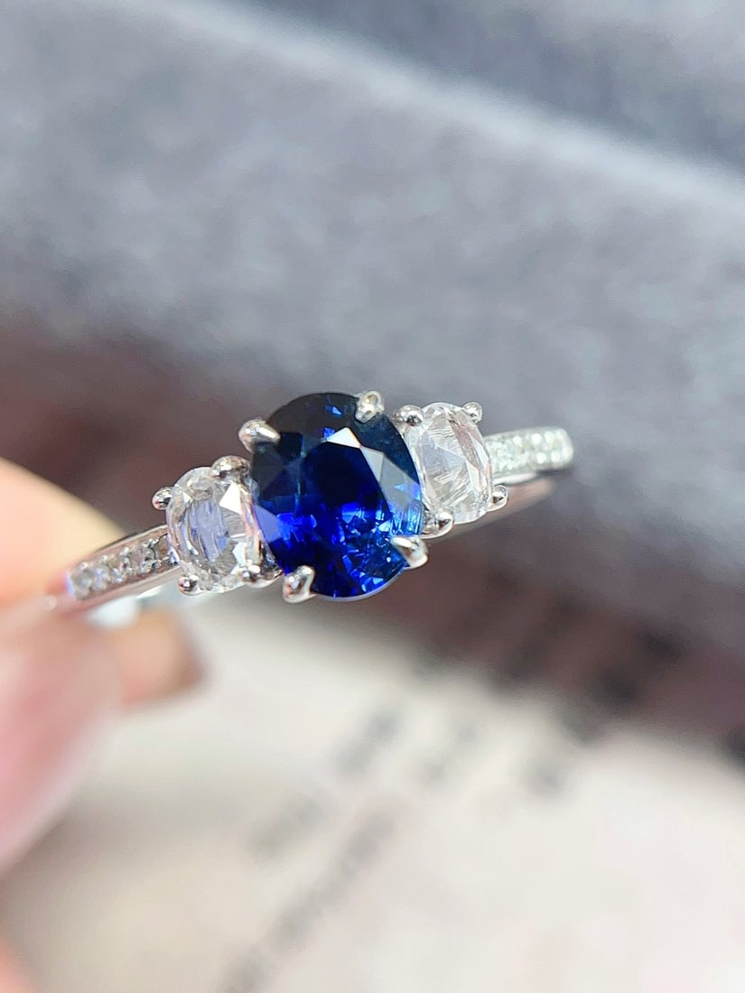 18K Gold Royal Blue Sapphire Ring: This ring is meticulously crafted in 18K gold, showcasing the noble hue of the royal blue sapphire. The main stone is clean and flawless, complemented by diamonds and white blue sapphires in an