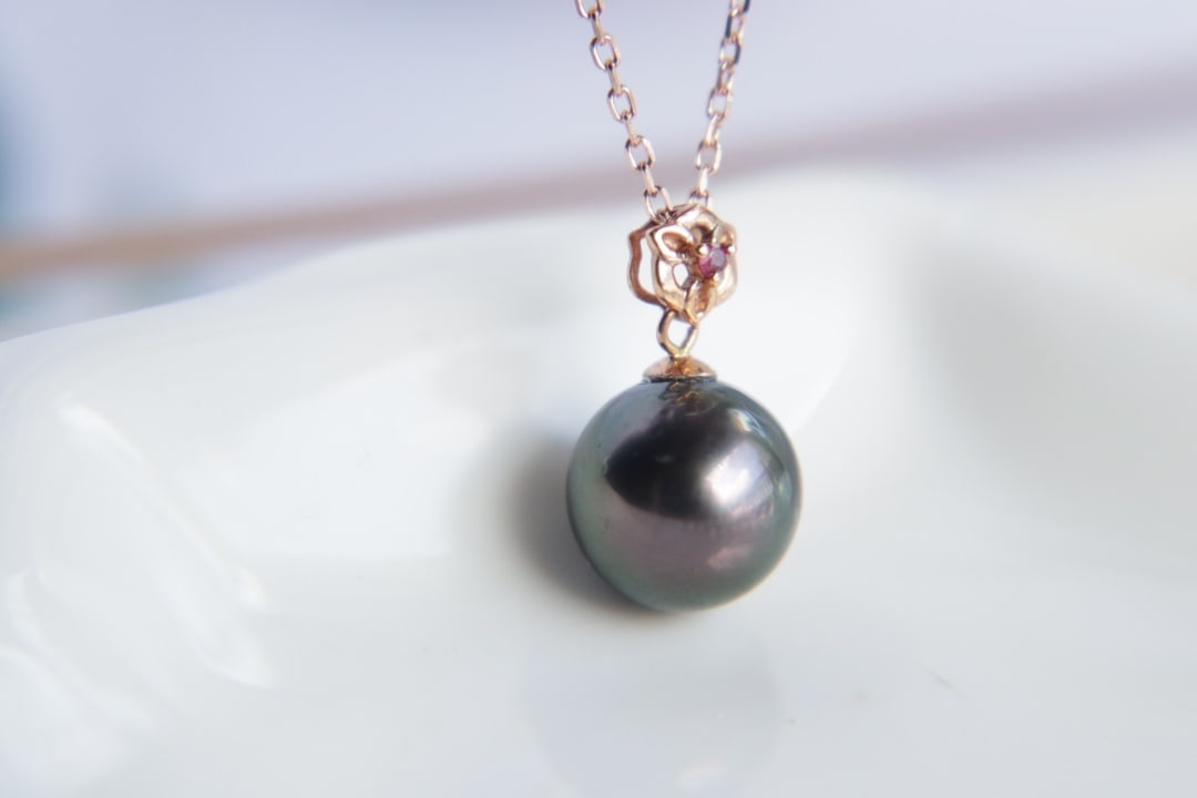 18K Gold Tahitian Pearl Pendant: This pendant is crafted from 18K gold, featuring a Tahitian pearl that showcases peacock green overtones and strong luster. The pearl's round shape and slight blemishes highlight its natural beauty.