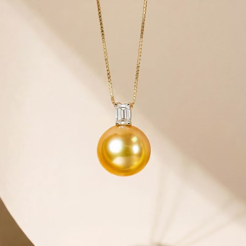 18K Gold South Sea Golden Pearl Pendant: This pendant is crafted in 18K gold, featuring a South Sea golden pearl with a rich tea-gold hue and mirror-like luster. The minimalist design exudes unique elegance. Paired with a 0.5-carat emerald-c