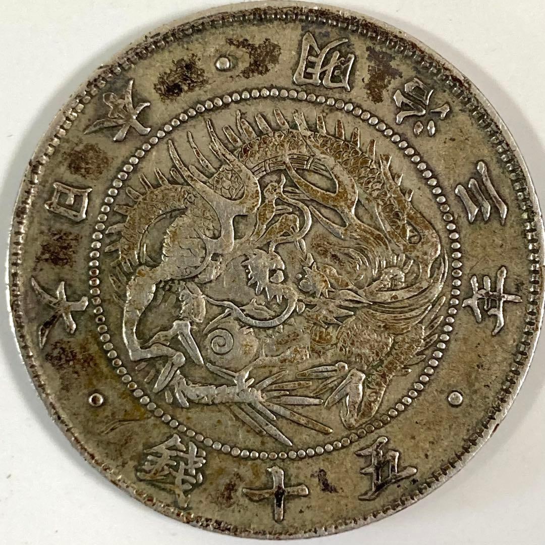 A large silver coin with a denomination of 50 sen from the 3rd year of the Meiji era (1870),: This is a slightly oxidized silver coin, characteristic of an antique coin.