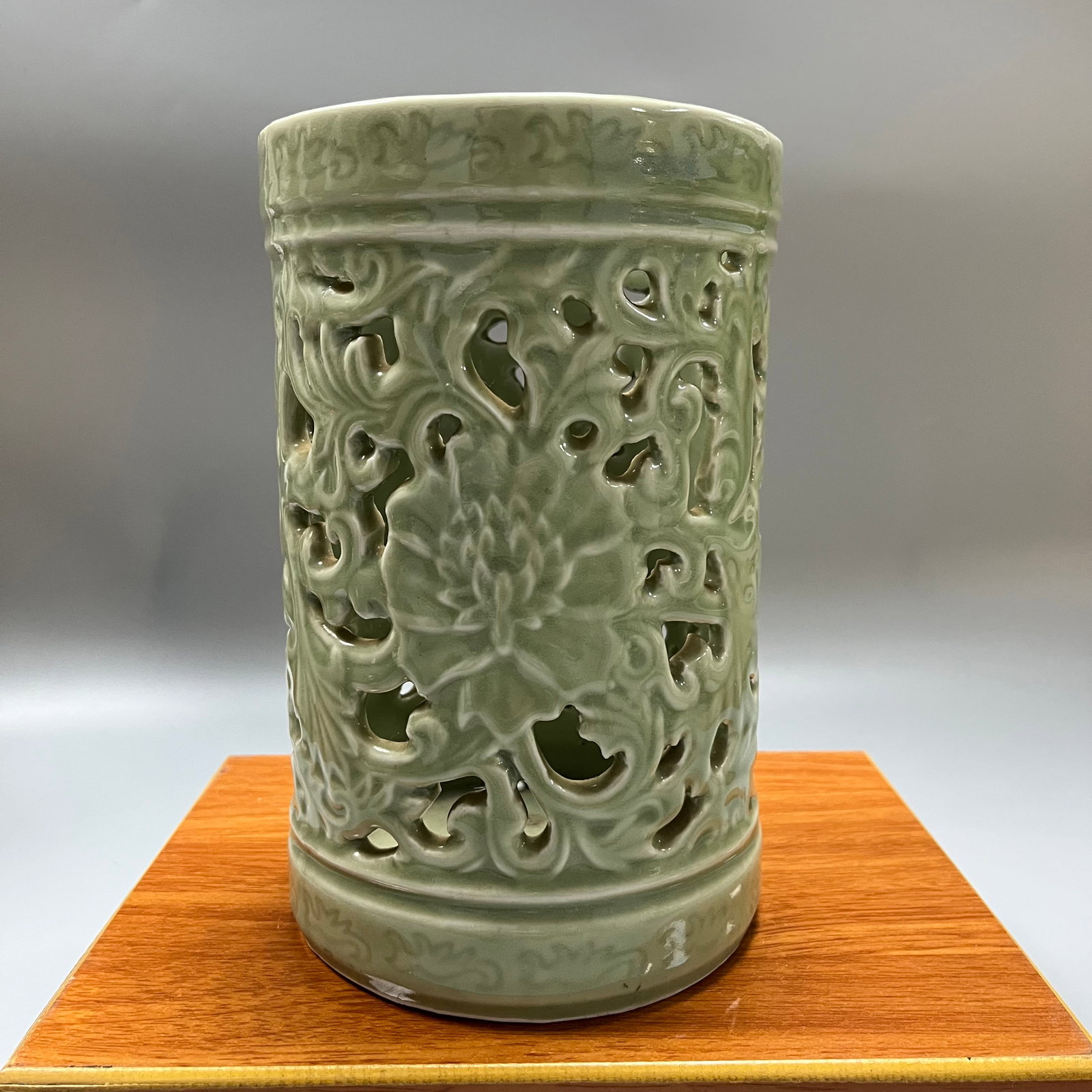 Qing Dynasty Celadon Glazed Openwork Lotus Scroll Pattern Porcelain Brush Pot: A Qing Dynasty celadon-glazed porcelain brush pot with openwork lotus scroll design, 23 x 14 cm. The brush pot is a standard cylindrical shape, covered entirely in a celadon glaze, the color of which