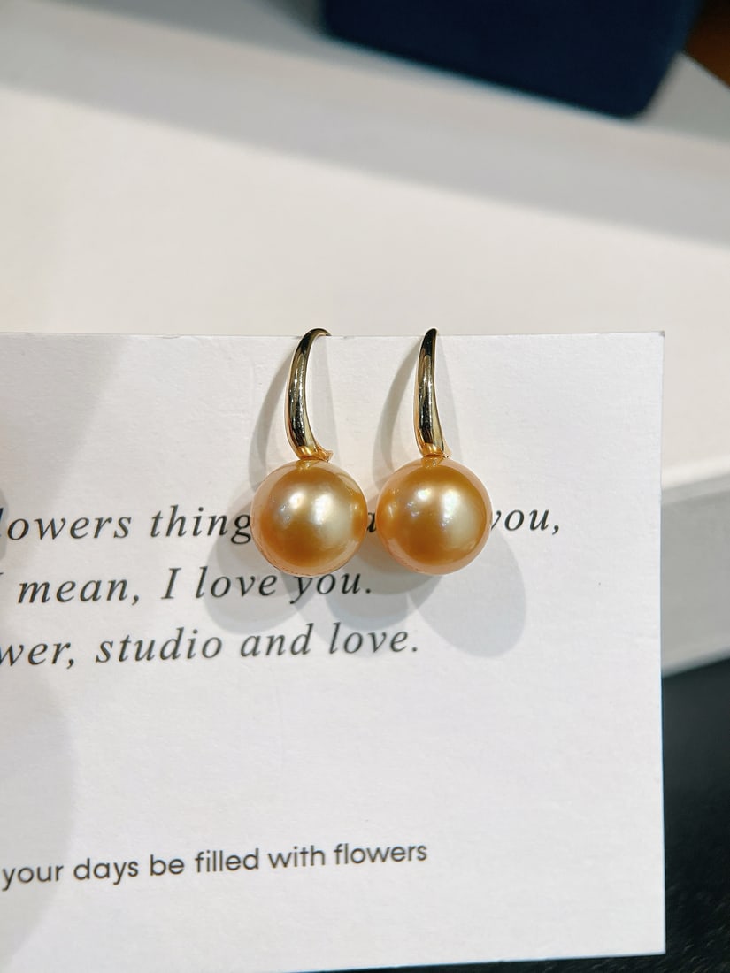18K Gold Classic Deep Golden Sea Pearl Earrings: These earrings feature classic deep golden sea pearls, paired with 18K gold hooks, showcasing a simple yet elegant style. The pearls have a diameter of 10-11mm, exhibiting a perfect round shape with s