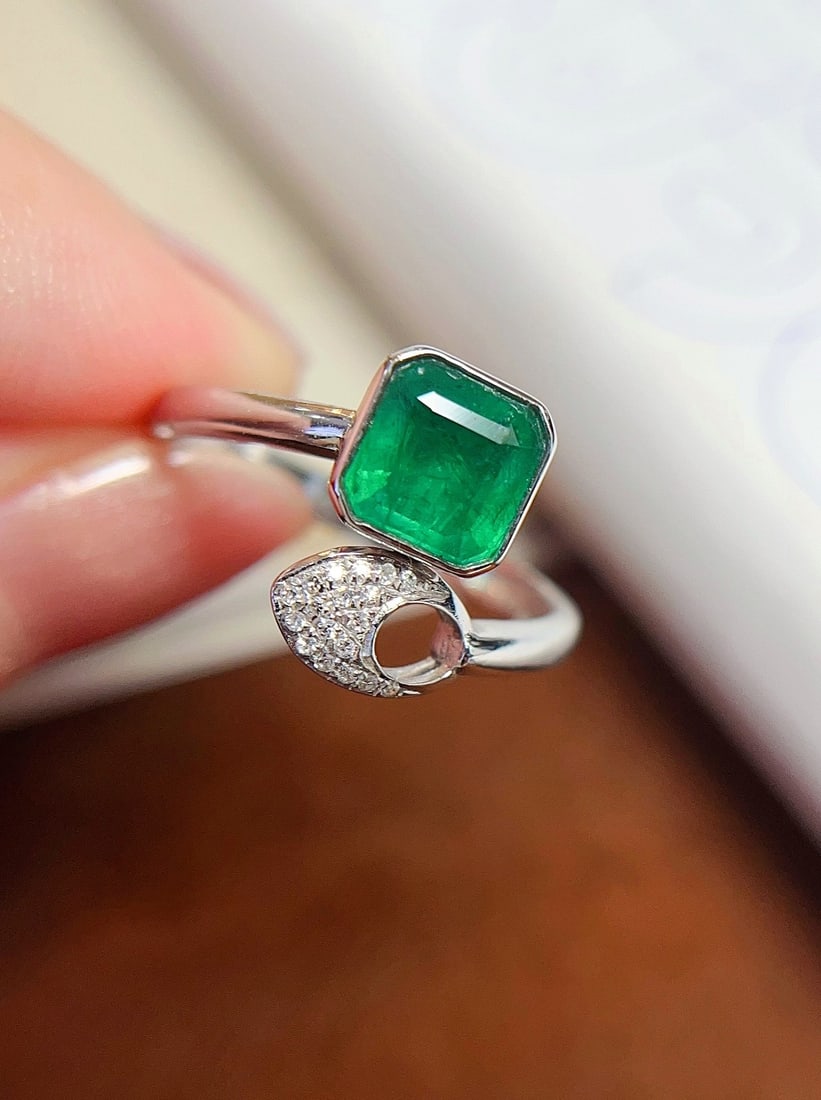 18K Gold Emerald Ring: This 18K gold ring features a princess-cut emerald with a rich hue, exuding a grand design and exceptional presence when worn. The flawless main stone complements the exquisite diamonds, highlighting 