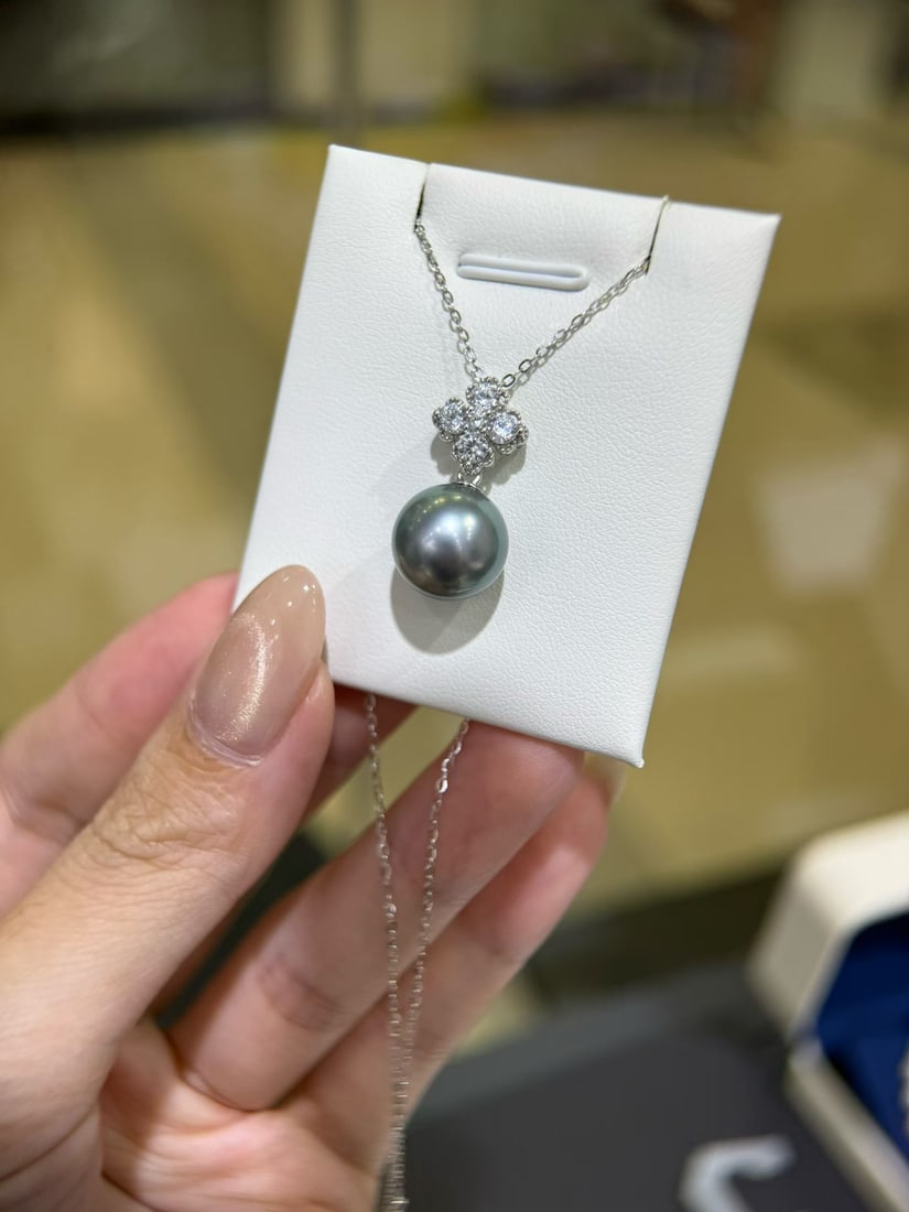 Platinum Natural Gray Pearl Pendant: This pendant features a Tahitian pearl as the main stone, showcasing a vibrant green luster with a smooth and delicate surface. The round shape has minor imperfections, exuding elegance. Paired with