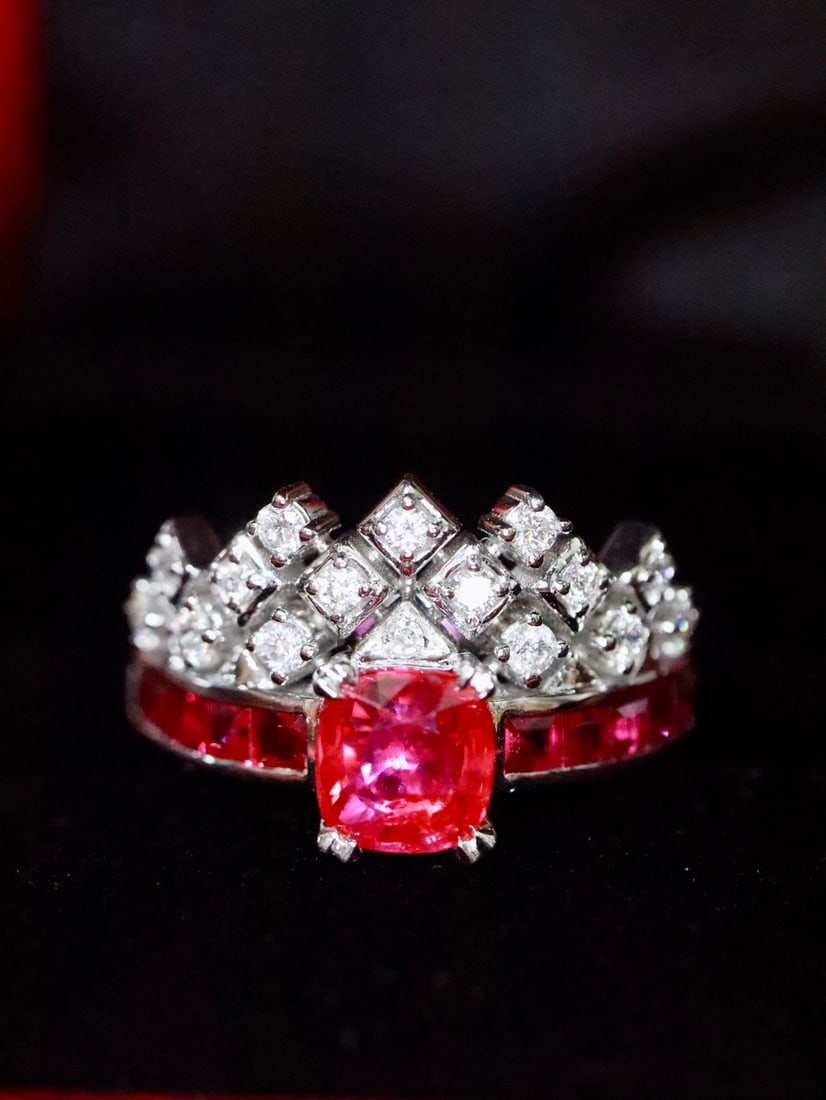 Platinum Natural Ruby Ring: The platinum setting outlines a delicate contour, with a vivid red gemstone radiating a unique glow. Surrounding diamond formations are neatly arranged, like guardians of the treasure, releasing