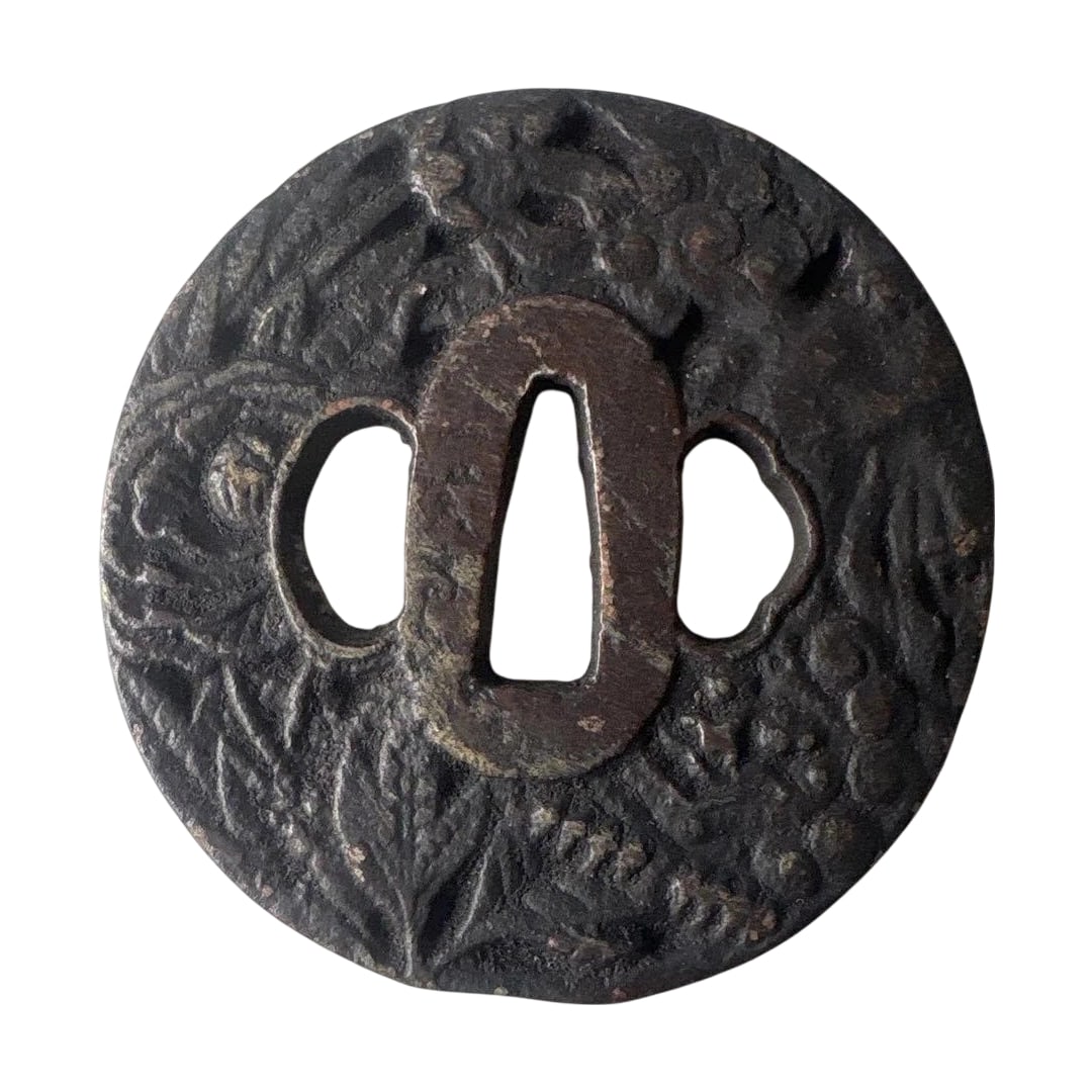 Metal Tsuba with Botanical Motif: Metal Tsuba with Plant Motif This is a metal tsuba (sword guard) engraved with a plant motif. It is circular in shape with three holes in the center. The material is metal with a blackened finish.