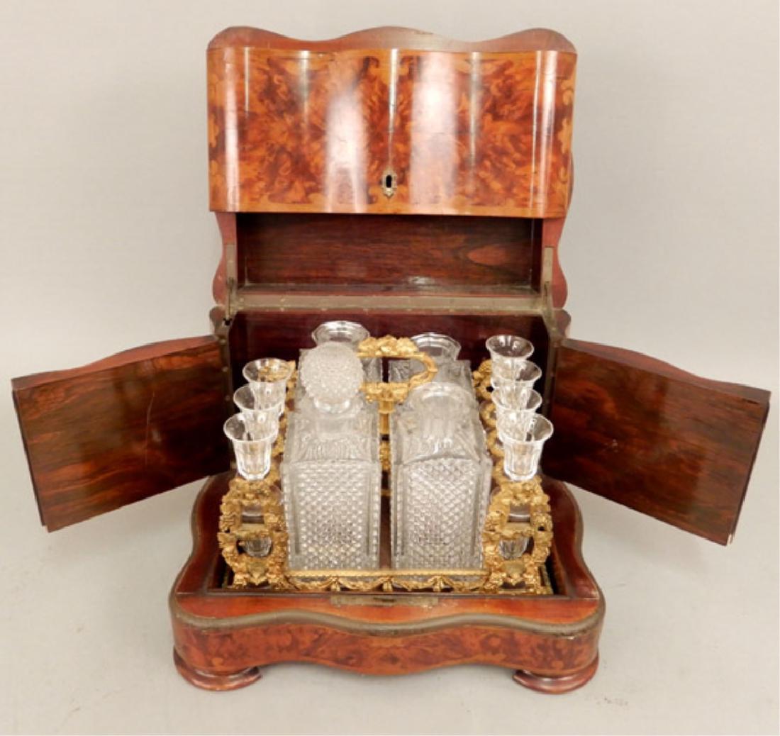 Inlaid mahogany tantalus set with decanters and: Inlaid mahogany tantalus set with decanters and stemware, engraved metal rims, hinged lid and sides, includes four decanters (only one stopper), and fourteen cordials (missing two), in a fitted wood a