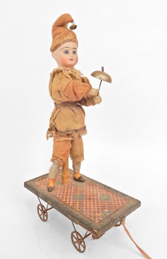 Automaton pull toy doll: Automaton pull toy doll, painted bisque head, wooden hands and legs, with blue glass eyes, open mouth with teeth, head turns and arm moves to strike bell as the wheels turn, mounted on pull toy, all o