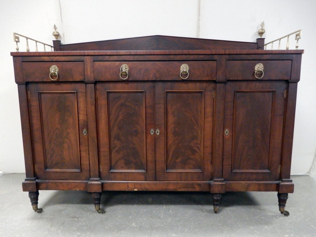 Federal mahogany sideboard: Federal mahogany sideboard, brass side galleries, brass finials, three short drawers, with four paneled doors below, turned legs on casters, 57" x 72 1/2" x 25"