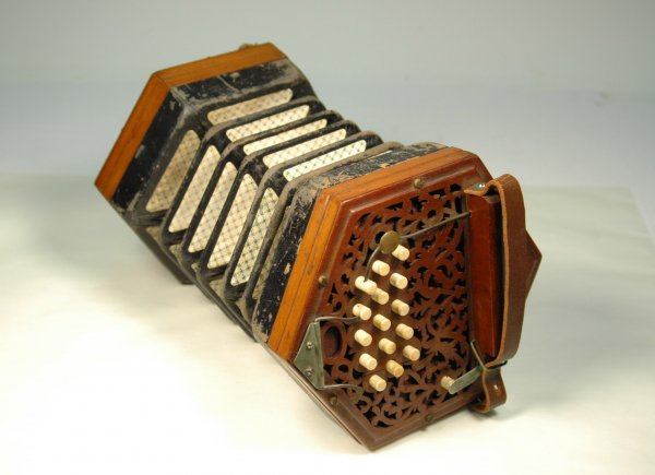 Concertina or squeeze box, with vertical case. Ela: Concertina or squeeze box, with vertical case. Elaborate carved filigree fretwork, with celluloid buttons. Stamped "Steel Reeds", late 19th C, missing one leather strap, a few splits in fretwork, tape