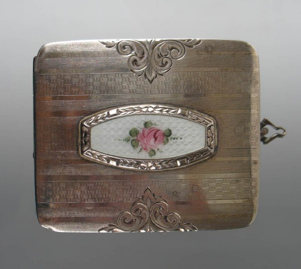 Enameled sterling silver compact with engraved des: Enameled sterling silver compact with engraved design, has ring to attach chain, center plaque with hand painted rose on white enamel background, 2 1/2" long x 2 1/8" wide, inside has coin holder, lip