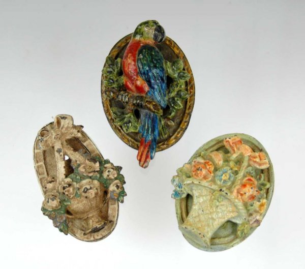 Three cast iron door knockers incl. 1) Flowers in : Three cast iron door knockers incl. 1) Flowers in woven basket, 2) Parrot on a branch, 3) Flower basket with large ribbon. Largest measures 5". All early to mid 20th C.