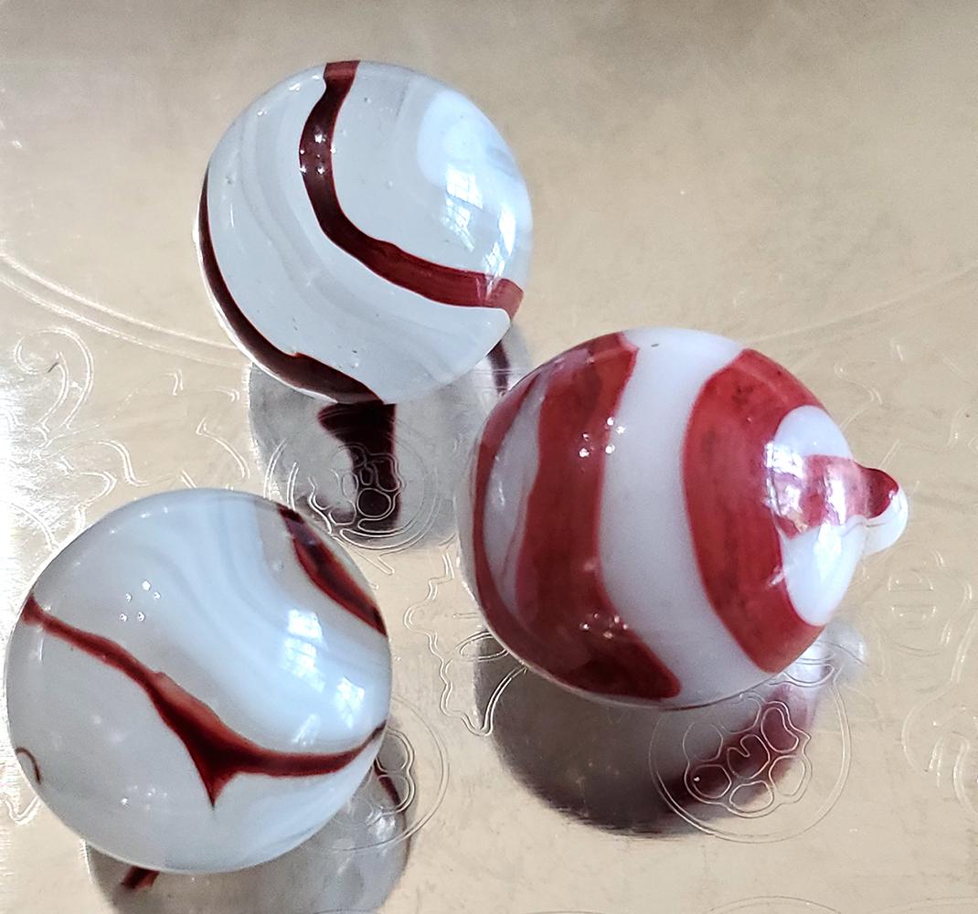 Three Vintage Oxblood Marbles: Three vintage oxblood marbles including one 17mm Akro "bloody nipple" and one 16mm silver oxblood corkscrew