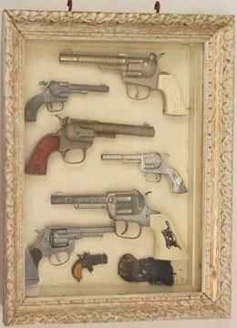 Shadow box display case with seven toy guns: Shadow box display case with seven toy guns, including Hubley, Rodeo, and Smoky, and a Davy Crockett medallion