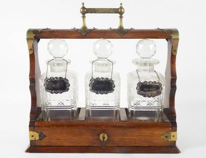 English Tantalus Liquor Bottle Set: English Tantalus liquor bottle set, fitted oak case holder with applied brass mounts and handle, three cut crystal glass liquor bottles, right side plate beneath handle is stamped "X1032", bottles