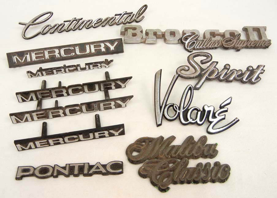 Grouping of eleven vintage automobile emblems incl: Grouping of eleven vintage automobile emblems including Pontiac, five Mercury, Volare, Spirit, Bronco II, Cutlass Supreme, Malibu Classic, and Continental