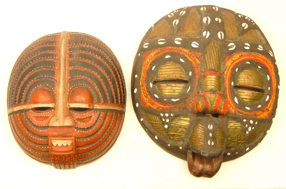 Two Oceanic masks, one with beadwork around eyes a: Two Oceanic masks, one with beadwork around eyes and on nose, allover white cowry shell and brasswork decoration on mud over wood mask, 17 1/2" x 14 1/4", and a painted wooden mask, New Guinea, 13 1/2