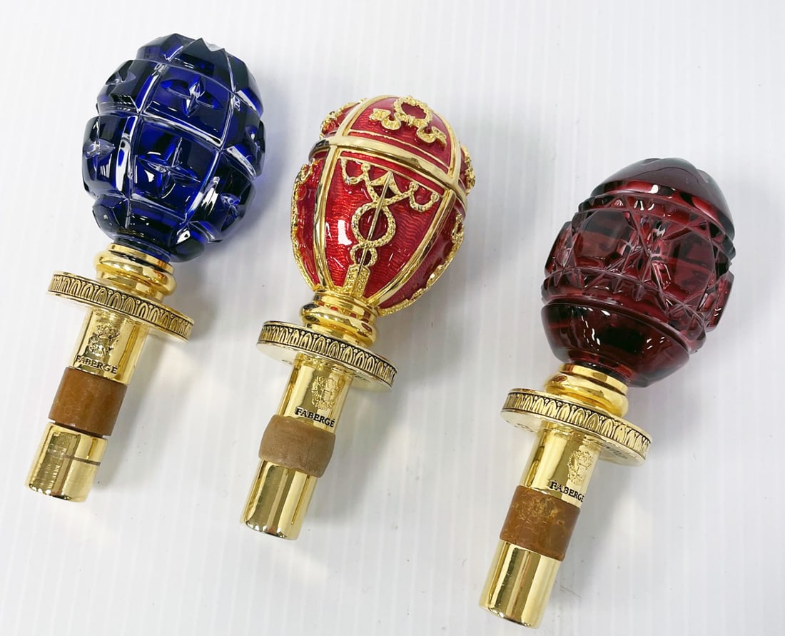 Faberge Wine Bottle Stoppers Grouping: Three piece Faberge wine bottle stoppers grouping, glass and enameled metal egg form tops mounted onto 24k gold plated metal stems, styled after Russian Imperial eggs, signed on stems FABERGE PATENTED