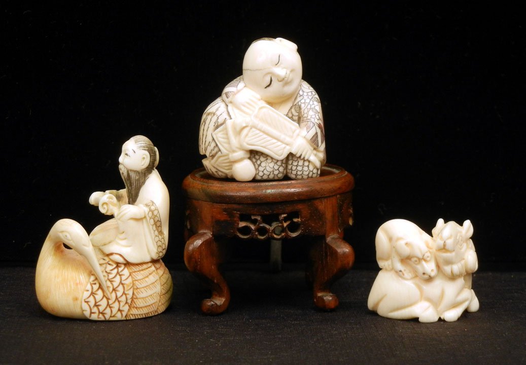 Two ivory netsukes and a carved ivory figurine, one: Two ivory netsukes and a carved ivory figurine, one of a seated ram with dog on its back, and one of an Asian man seated on bird, artist signed on bottom, figurine of seated man holding fan, signed on