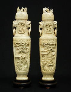 Pair of Chinese carved ivory figural covered urns,: Pair of Chinese carved ivory figural covered urns, both with ring handles on each side with foo dog heads, figural village scenes on both sides, figures carved on lids, both with wooden bases, China C