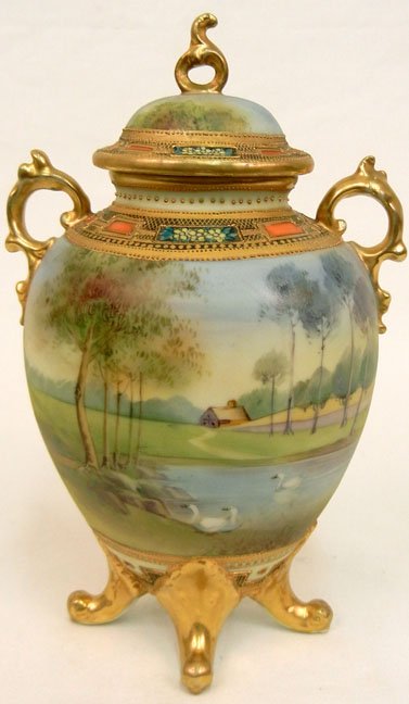 Hand painted Nippon covered urn, landscape scene with s: Hand painted Nippon covered urn, landscape scene with swans on a lake and house in background, gilt decoration, blue mark on bottom, double handled, footed base, finial top, 9 1/4" high