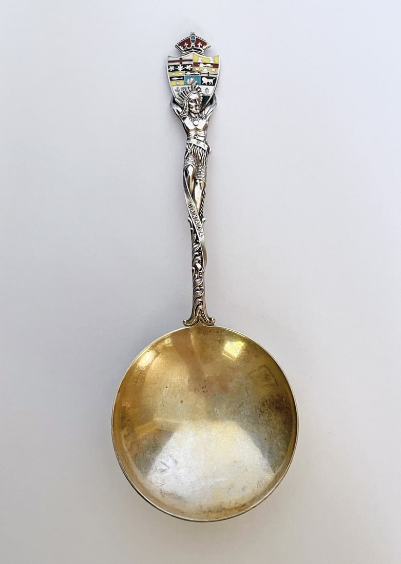 Sterling Silver Canadian Collector's Spoon: Sterling silver Canadian collector's spoon, full figure of Native American Indian holding enameled crest, round bowl with gold wash, 8" long, stamped Sterling 925 with English hallmarks, weight 2.23 o